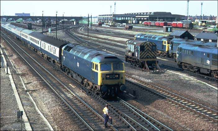A class 47 comes into Peterborough past the small Depot with a platelayer stood on the down fast.